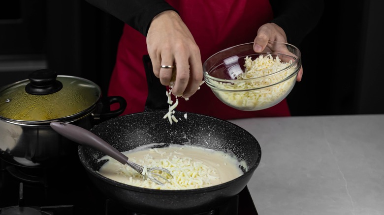 sprinkling shredded cheese into saucepan