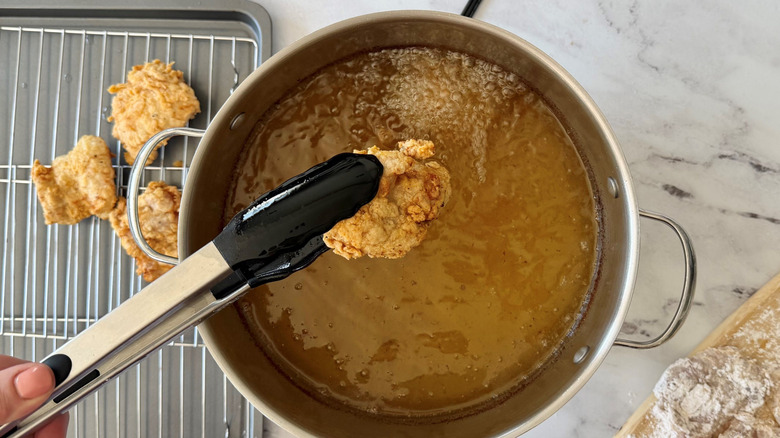 Tongs removing fried chicken from oil