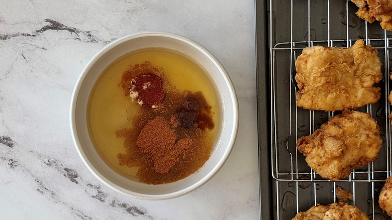 Oil and seasonings in bowl next to rack of fried chicken