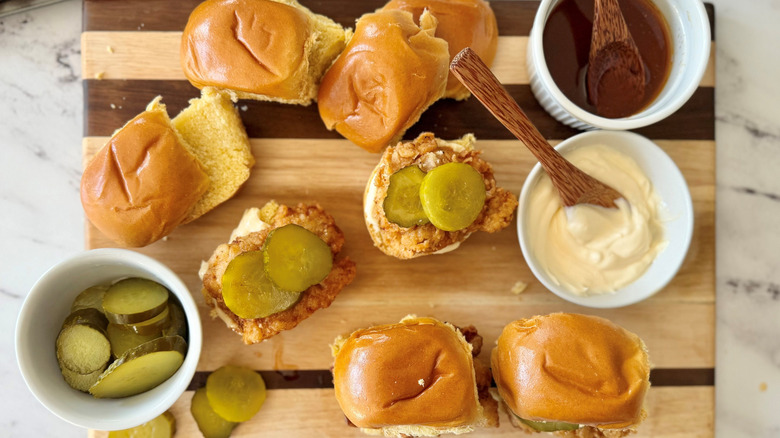 Nashville hot chicken sliders on wooden board with mayo, pickles, and seasoned oil