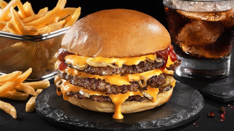 Triple cheeseburger oozing with American cheese alongside fries and soda