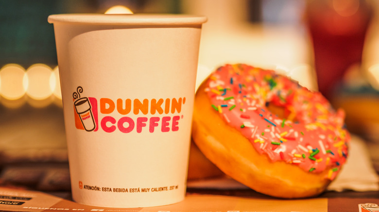 Dunkin' paper coffee cup and pink sprinkled donut