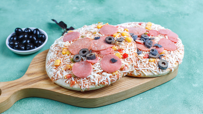 Two frozen pizzas on wooden slab