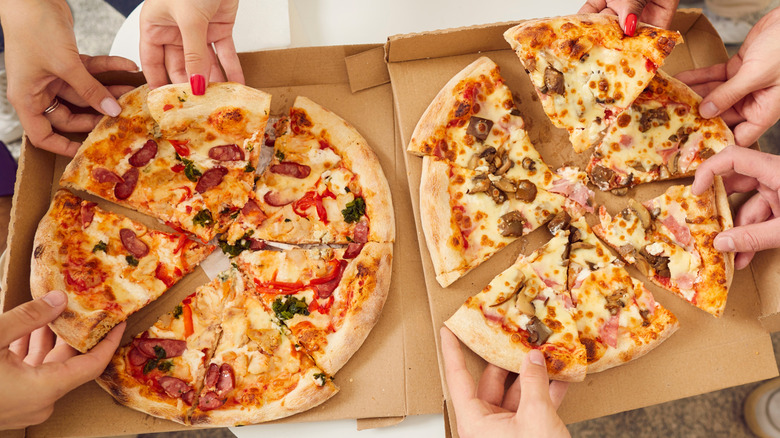 Hands pulling slices from two pizza boxes
