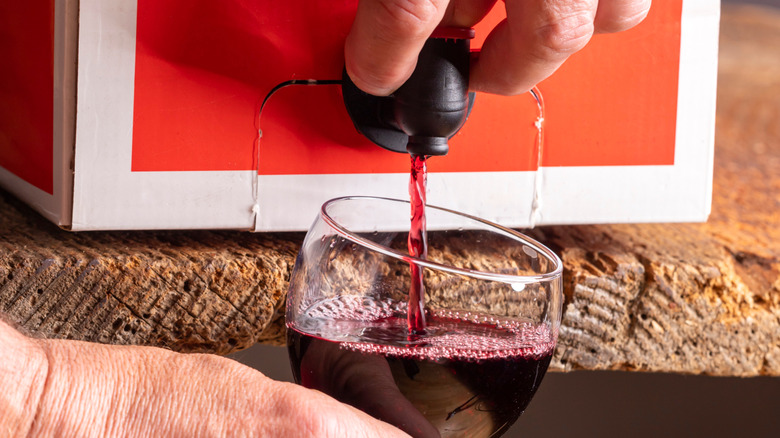 Person dispensing boxed red wine into glass.