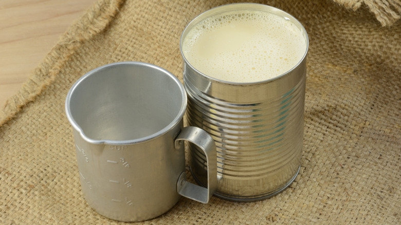 Can of condensed milk beside an old-fashioned measuring cup