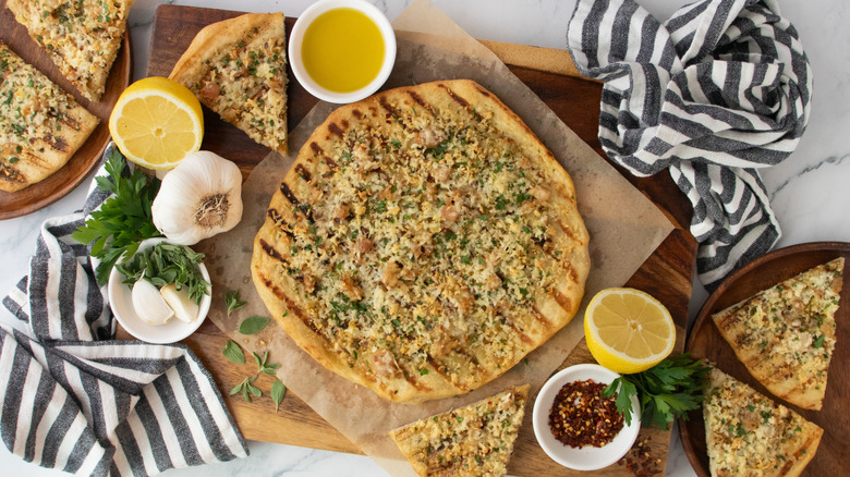 White clam pizza surrounded by lemons, garlic, herbs, and chili flakes