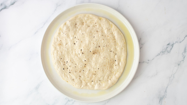 Pizza dough seasoned with salt and pepper on plate