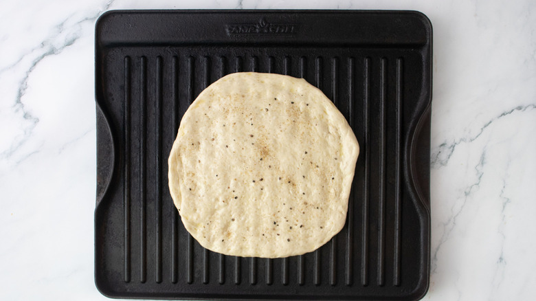 Seasoned pizza dough on grill pan