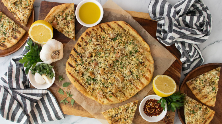 White clam pizza surrounded by garlic, lemons, oil, red pepper flakes, and more slices of pizza