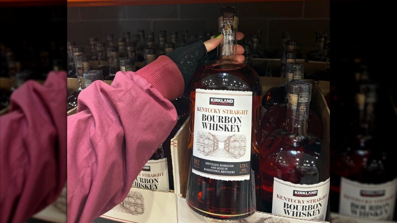 Hand grabbing a bottle of Kirkland Signature Kentucky Straight Bourbon Whiskey