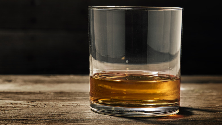 Glass of neat bourbon on a wooden surface.