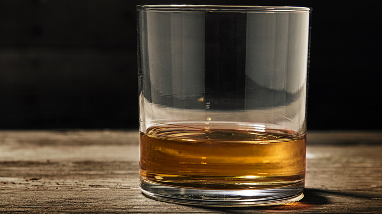Glass of neat bourbon on a wooden surface.