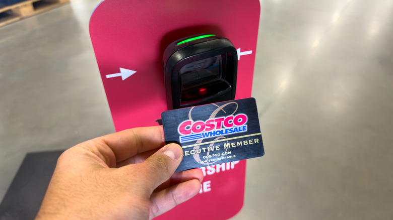 Hand holding a Costco membership card in front of scanner