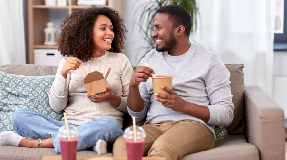 A couple enjoys their restaurant food at home on the sofa