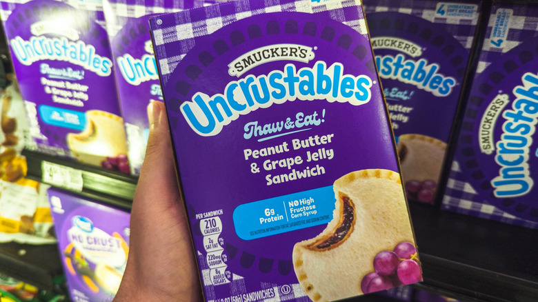 A hand holding up a box of grape Uncrustables.