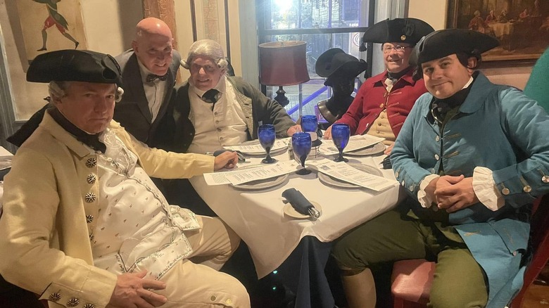 People in Colonial dress around table with blue glasses