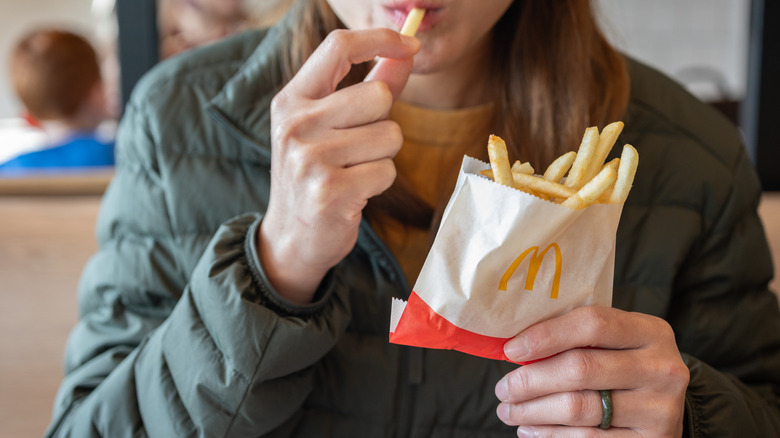 Person eating a french fry from a small paper bag with the McDonald's logo.