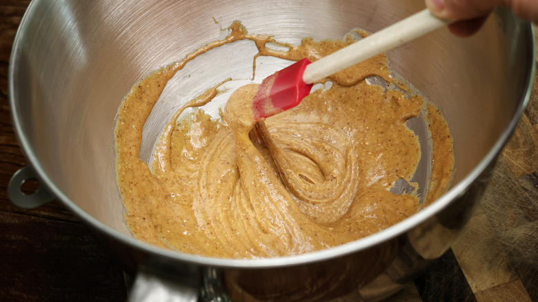 silicone spatula lifting out of mixture of almond butter and honey in a metal mixing bowl