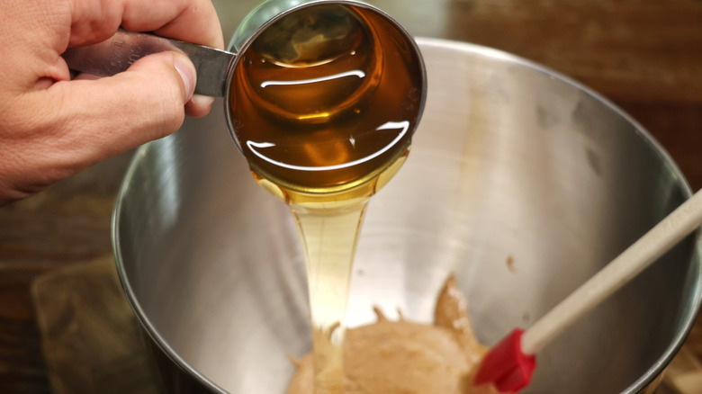 measuring cup of honey pouring into mixing bowl with almond butter in it