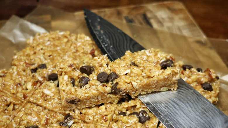 A chef's knife with a cereal bar resting on it atop a tray of sliced cereal bars