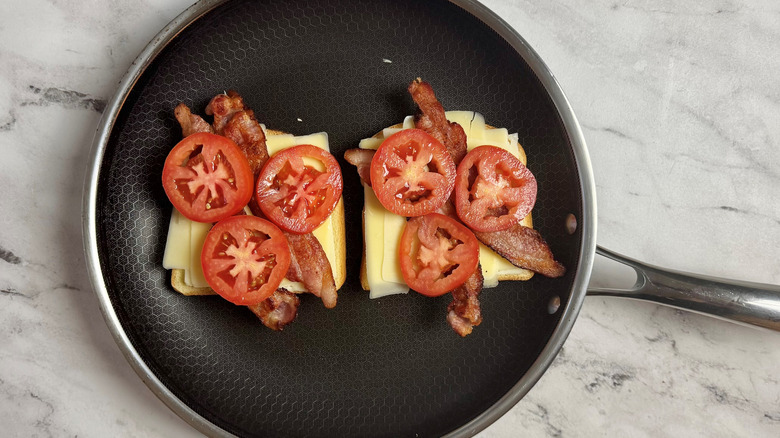bread covered with sliced cheese, tomatoes, and bacon in a frying pan
