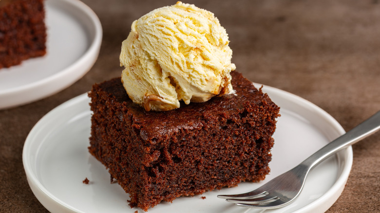 Chocolate cake on white plate with metal fork and vanilla ice cream scoop on top