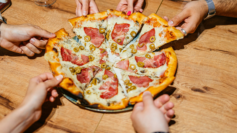 Pulling apart slices from a pizza with olives and ham.