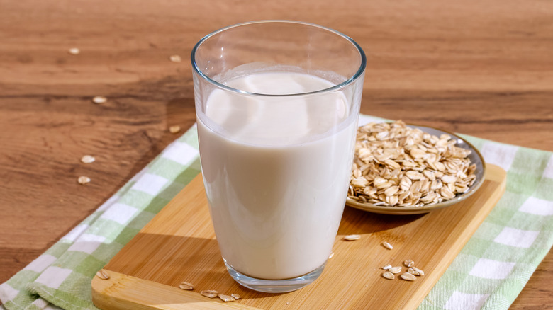 Glass of oat milk next to plate of raw oats.