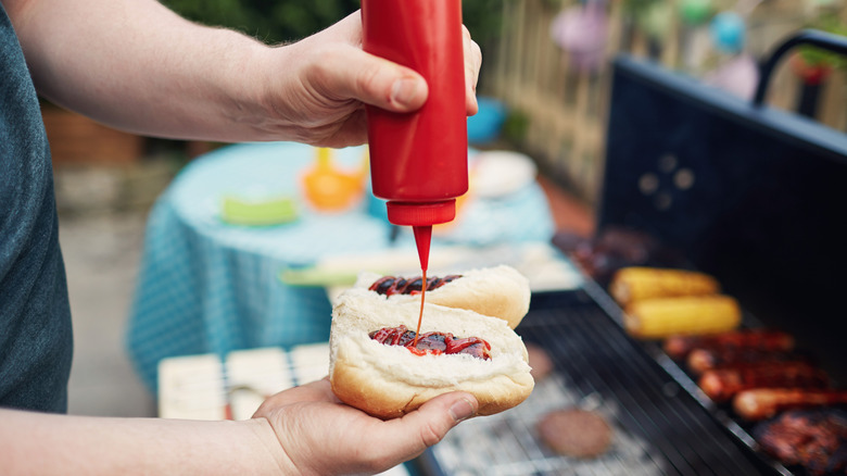 person putting ketchup on hot dogs at cookout