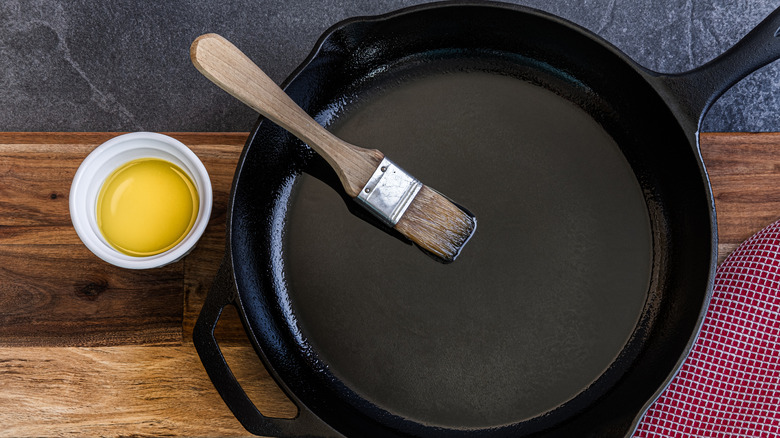 Small bowl of oil and brush with cast iron skillet on wood surface.