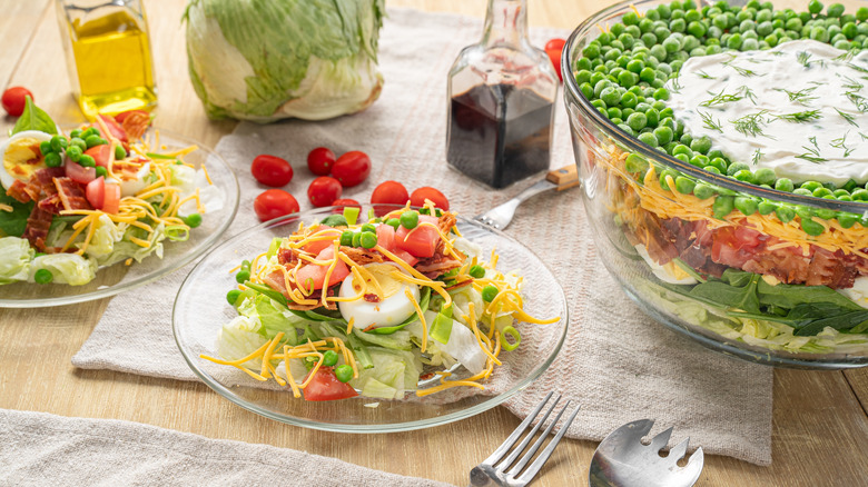 Retro veggie dish of iceberg lettuce, eggs, shredded cheese, and peas in a trifle bowl and some on glass plates