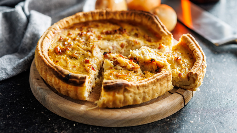 Quiche Lorraine with two slices taken out sitting on a round, wooden cutting board