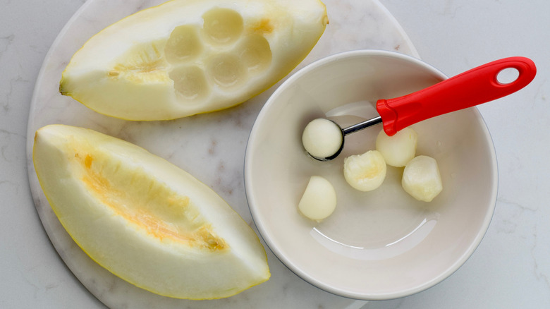 melon baller with slices of melon and melon balls in a bowl