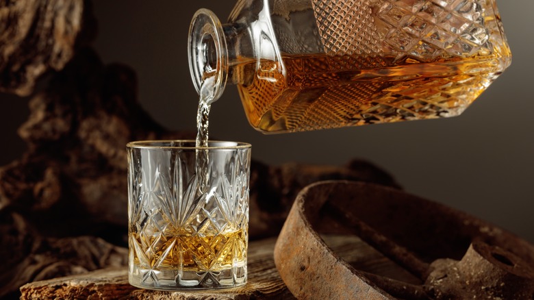 glass of whiskey being poured on a wooden board and wheel