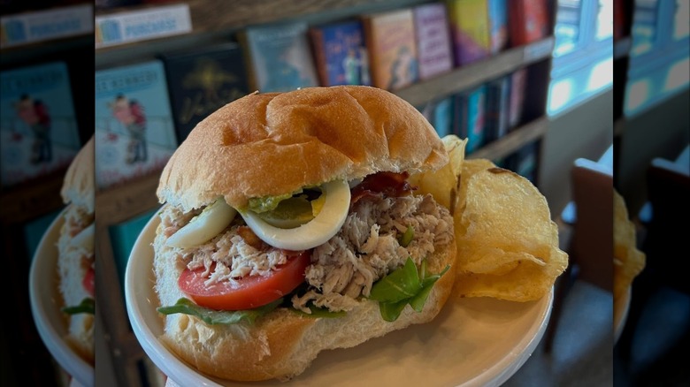 A Cobb salad sandwich served with potato chips on a white plate