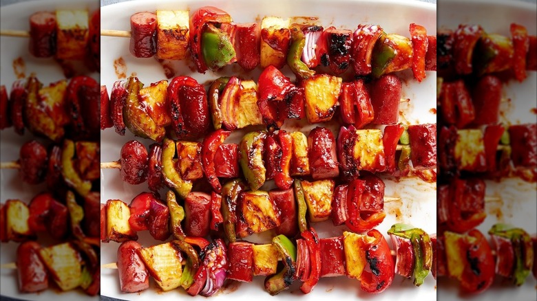 Skewers loaded with hot dog, peppers, pineapple, and onion on a white serving dish