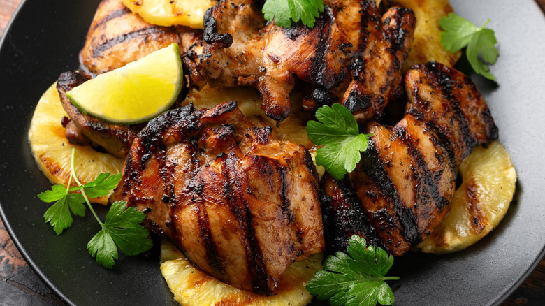 Huli huli chicken on a bed of pineapple garnished with lime and herbs