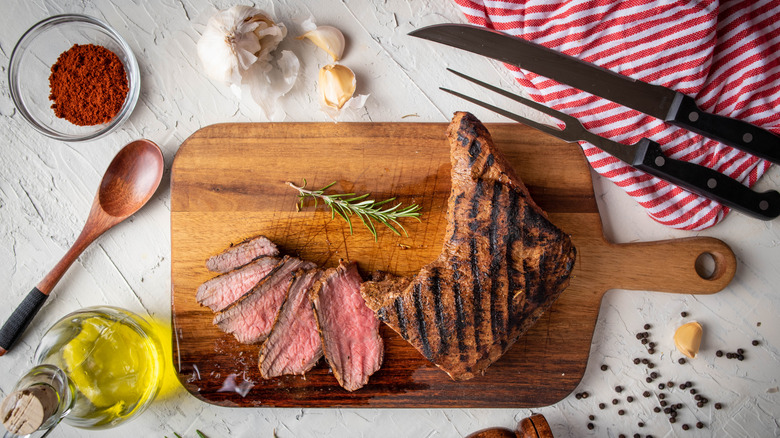 Santa Maria-style barbecue steak on a cutting board with herbs, garlic, oil, and cooking utensils