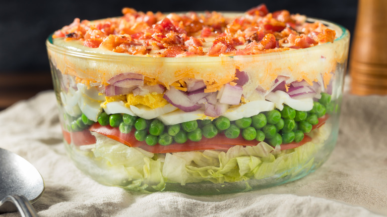 Seven-layer salad in a large glass bowl next to a spoon