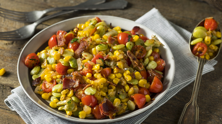 A bowl of succotash next to forks and a spoon full of succotash
