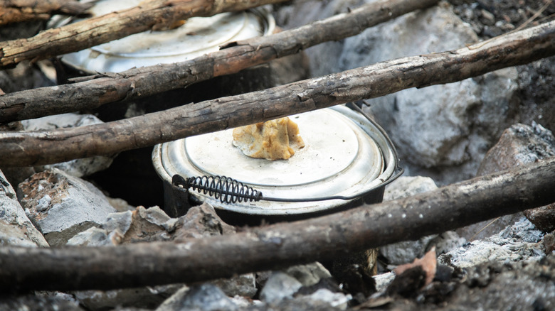 Metal pot over in-ground fire pit surrounded by rocks and wood