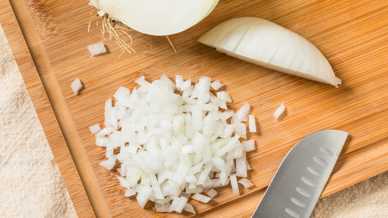 Diced white onions and a knife on a wooden cutting board