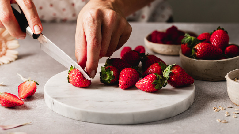 A close-up of a hand cutting strawberries on a marble cutting board