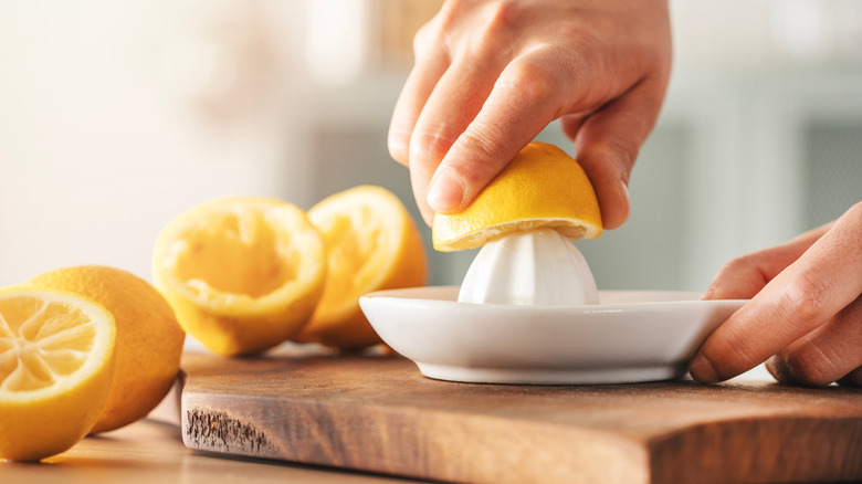 A hand squeezing out lemon juice with a juicer on a wooden cutting board