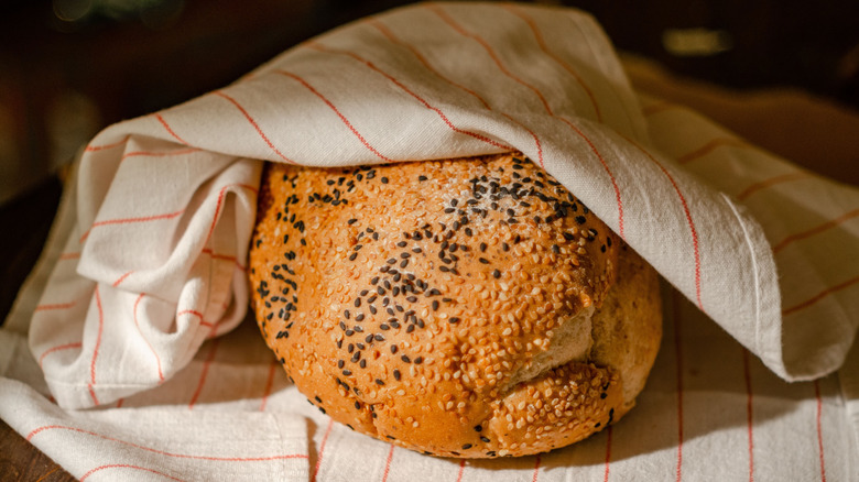 A loaf of sesame bread wrapped in a tea towel