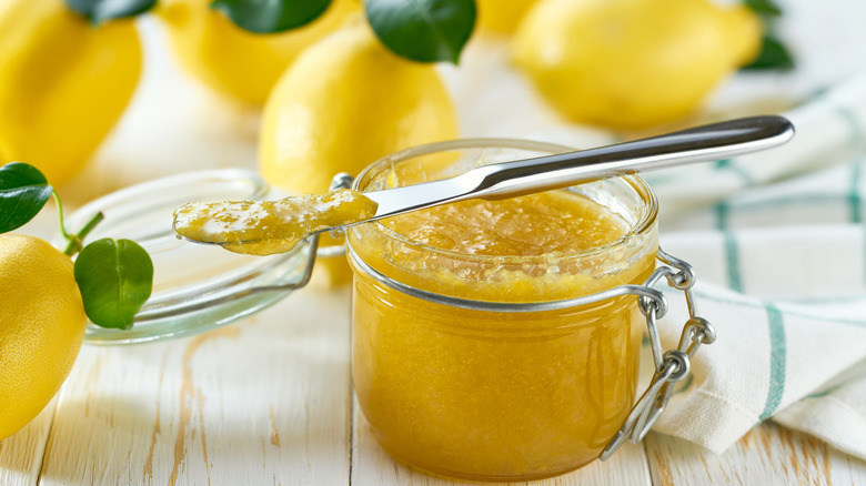 A jar of lemon preserve next to fresh lemons