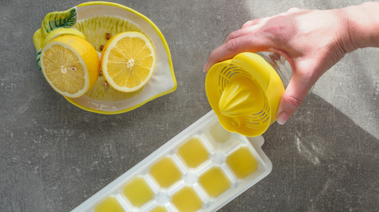 A halved lemon in a dish next to a hand pouring lemon juice into an ice cube tray