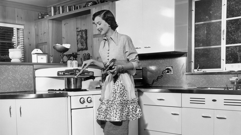 A 1950s woman in an apron cooking at a stove