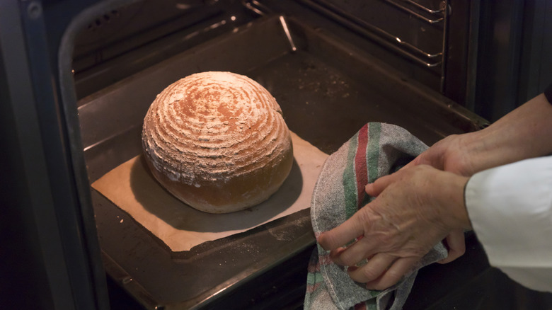 Someone removing a loaf of bread from their oven using a dish towel